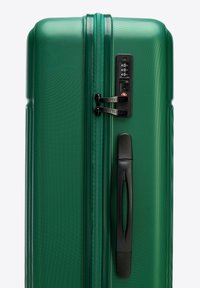 Hard-shell green suitcase with a textured exterior, dual zippers, built-in combination lock, and a retractable black handle.