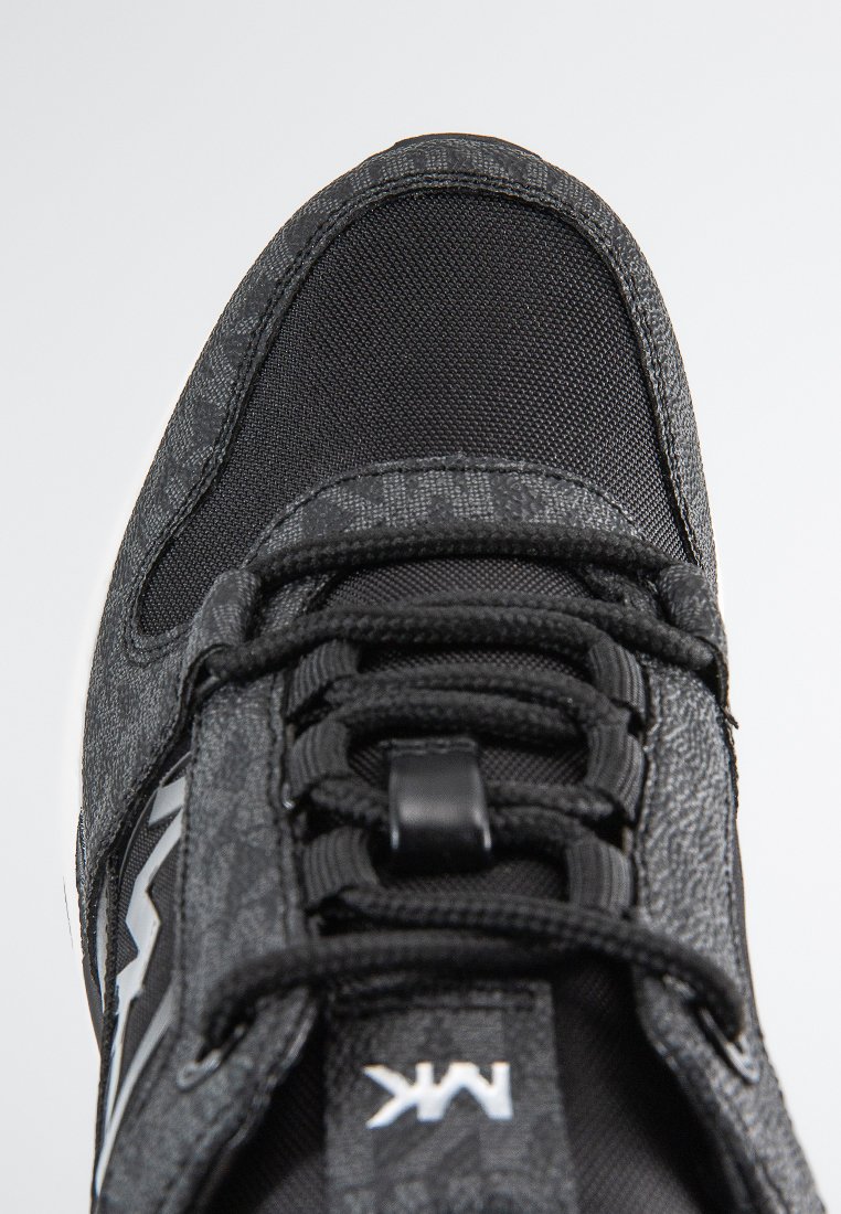 Zwarte sportieve schoen van mesh en gestructureerde stof, met platte veters en een platte zool. Accenten zijn onder andere een zilveren logo aan de zijkant.