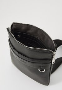 Sac bandoulière en cuir noir avec un extérieur texturé, une fermeture éclair argentée et plusieurs compartiments intérieurs pour un rangement organisé.