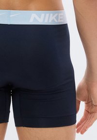 Κοντινό ενός ατόμου που φοράει σκούρο μπλε ανδρικά μποξεράκια Nike με ανοιχτό μπλε μέση που φέρει το λογότυπο Nike και το σύμβολο swoosh.