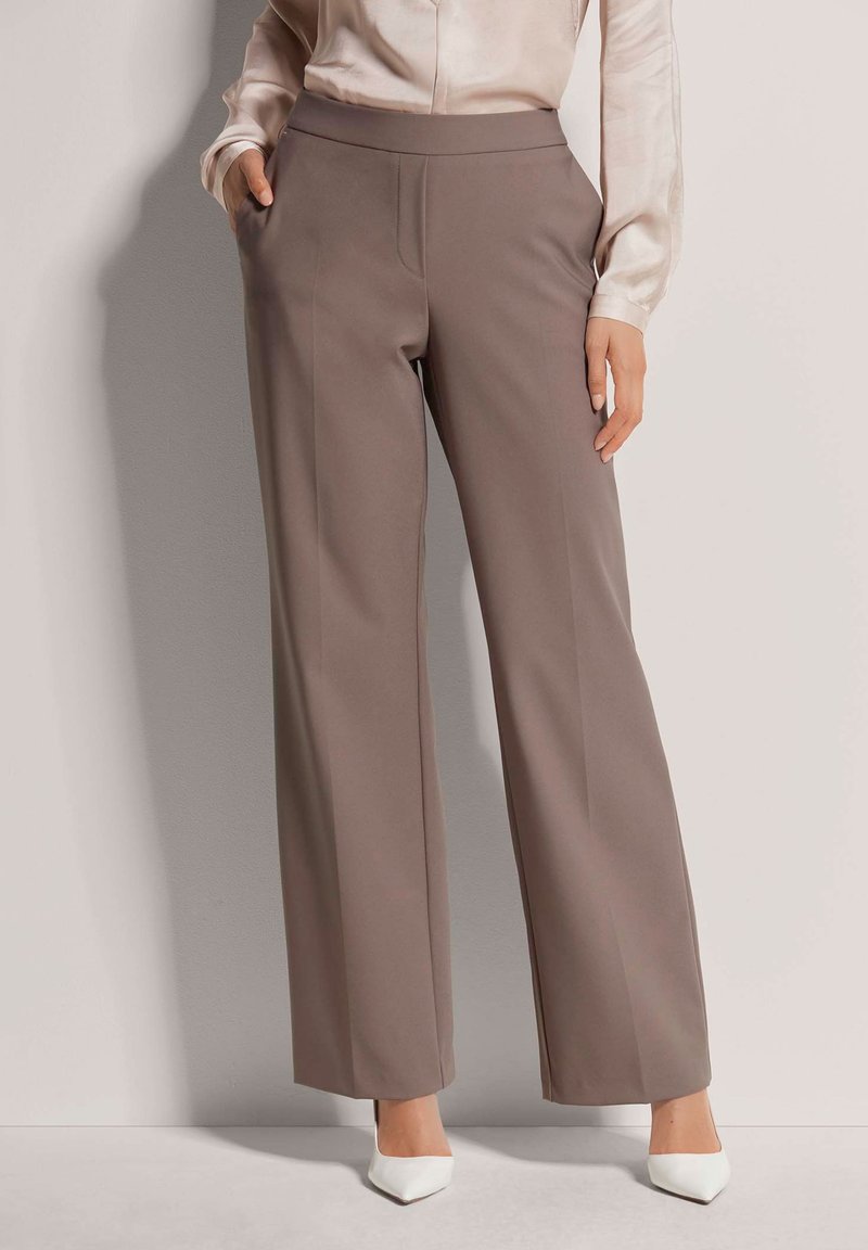 Brede broekspijpen in taupe stof, met een hoge tailleband, zijzakken en een gladde textuur, gecombineerd met witte puntige hakken.