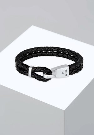 Schwarzes, geflochtenes Lederarmband mit einem silbernen Verschluss im Schlaufendesign. Glatte Textur, minimalistischer Stil und graviertes Logo auf dem Verschluss.