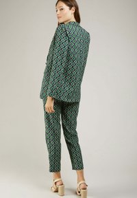 Costume à motif géométrique vert et bleu avec des manches longues, pantalons ajustés et sandales à talons blocs. Comprend un col cranté et un tissu texturé.