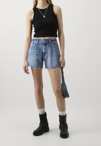 Musta lyhyt toppi, korkeavyötäröiset farkkushortsit, kulunut sininen sävy, rispaantunut helma. Mustat nilkkurit ja pieni sininen olkalaukku. Valkoiset sukat.