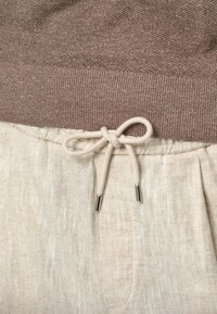 Brun stickad överdel med ribbad struktur ovanför beige linnebyxor, med elastisk midja och ljusfärgad snodd som är knuten i en rosett.