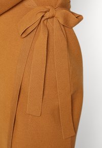 Maglione color ruggine caratterizzato da un grande fiocco realizzato con lo stesso tessuto lavorato a maglia, con una texture liscia e una forma aderente.
