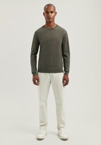 Olijfgroen gebreid sweater met lange mouwen, ronde hals en geribbelde manchetten, gecombineerd met witte rechte broek en witte sneakers.