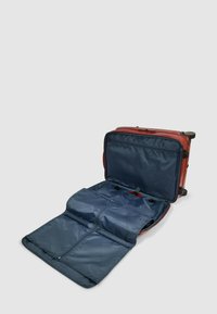 Rode koffer op wielen geopend, met een marineblauwe binnenkant met ritssluitingen en riemen. Gladde buitenkant met stevige wielen en handvatten.