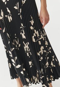 Gonna plissettata nera con un motivo floreale beige. Il tessuto ha una consistenza morbida e il design presenta foglie grandi e piccole alternate.