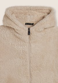 Giacca in pile beige con zip, dal morbido e soffice tessuto e un cappuccio. Presenta una zip nera e un'etichetta all'interno del colletto.