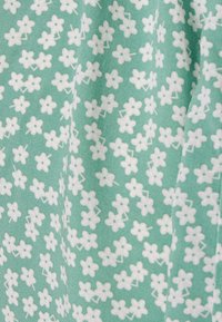 Tecido verde com um pequeno padrão floral branco. O material parece suave, com uma ligeira textura e detalhes distribuídos uniformemente por toda a extensão.