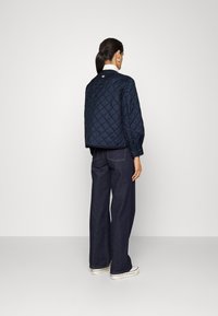 Giacca trapuntata blu navy con design corto e maniche lunghe, abbinata a jeans larghi blu scuro e sneakers bianche.