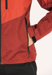 Röd och vinröd vadderad jacka med en zip-ficka, med en texturerad tyg och kontrasterande svart dragkedja och kardborre detaljer.