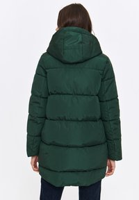 Zielona kurtka puchowa z kapturem, z pikowanymi sekcjami, gładką teksturą i długością do kolan. Brak widocznych zapięć z tyłu.