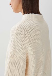 Maglione lavorato a maglia color crema con colletto alto, motivo testurizzato e spalle scese, che presenta una vestibilità ampia e un tessuto morbido.