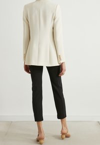 Cream tailored blazer with gold buttons, paired with black fitted trousers. The blazer has a structured shape and smooth texture.