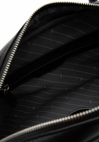 Interno di una borsa in pelle nera con una texture liscia, caratterizzato da una fodera in tessuto scuro con un motivo e una chiusura con zip in argento.