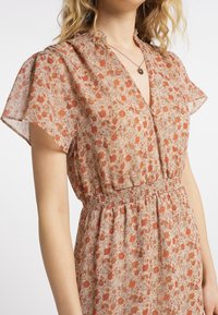 Robe imprimée florale avec des manches courtes à volants, un décolleté en V profond et une taille smockée. Le tissu est léger et semi-transparent avec des tons orange et beige.