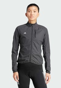 Lekka czarna kurtka z wysokim kołnierzem, przednim zamkiem błyskawicznym i zamkniętą kieszenią na piersi. Posiada białe logo Adidas oraz teksturowany materiał.