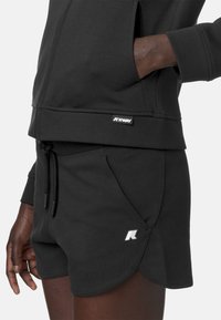 Felpa nera in misto cotone con tasca con zip e cordoncino, abbinata a pantaloni corti neri con orlo curvo e logo.