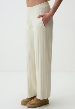 Pantaloni larghi color crema con texture a righe verticali, dotati di tasche laterali e una vita elastica. Abbinati a sneakers color cuoio.