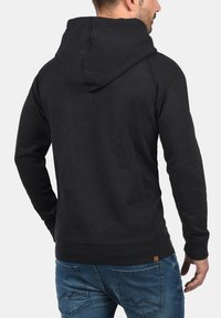 Black hooded sweatshirt with a textured finish, featuring a pouch pocket and ribbed cuffs. Back view displays a relaxed fit and minimalist design.