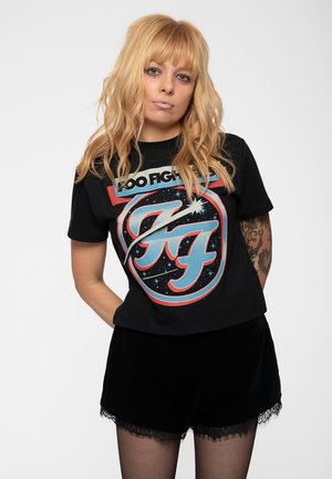 Black cropped t-shirt with a colorful retro graphic reading "Foo Fighters" and segmented "F" in blue and red. Paired with black velvet shorts.