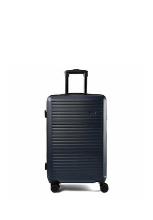 Valise rigide bleu foncé avec des rainures horizontales, poignée rétractable étendue et quatre roues pivotantes sur fond blanc.