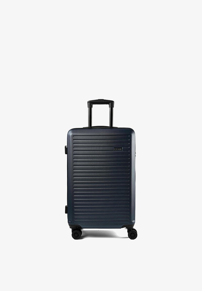 Valise rigide bleu foncé avec des rainures horizontales, poignée rétractable étendue et quatre roues pivotantes sur fond blanc.