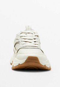 Sneaker bianca realizzata in pelle e rete, con una tomaia testurizzata, suola in gomma e suola esterna marrone a contrasto, lacci e branding minimale.
