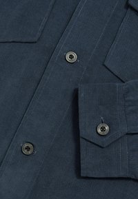 Navyblaue Cordhemd mit Point Kragen, zwei Brusttaschen und Knopfdetails mit Metallakzenten. Strukturiertem Stoff mit Rillen.