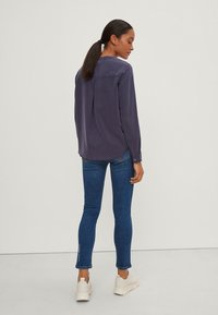 Blusa navy a maniche lunghe con una piega sul retro, abbinata a jeans blu aderenti e sneakers chiare. Tessuto liscio, design semplice.