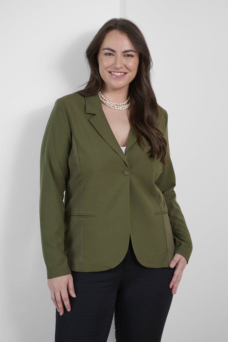 Blazer vert olive avec une fermeture à un bouton, des revers en pointe et deux poches avant ; associé à un pantalon sombre et un collier en perles.