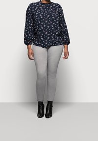 Marinblus med vitt blommönster, långa ärmar och rynkad halsringning, kombinerat med grå smala jeans och svarta ankelstövlar.