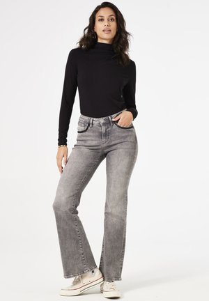 Un haut noir à manches longues associé à un jean en denim clair et évasé. Le jean dispose de poches avant et de surpiqûres contrastantes, porté avec des baskets blanches.