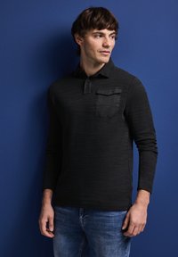 Czarna koszula polo z długim rękawem o teksturowanym wykończeniu, z kieszonką na piersi i klasycznym kołnierzykiem, połączona z niebieskimi dżinsami.