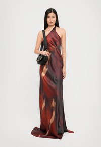 Halter-neck red and black maxi dress with a fluid silk-like design featuring abstract patterns, paired with a small black bag.