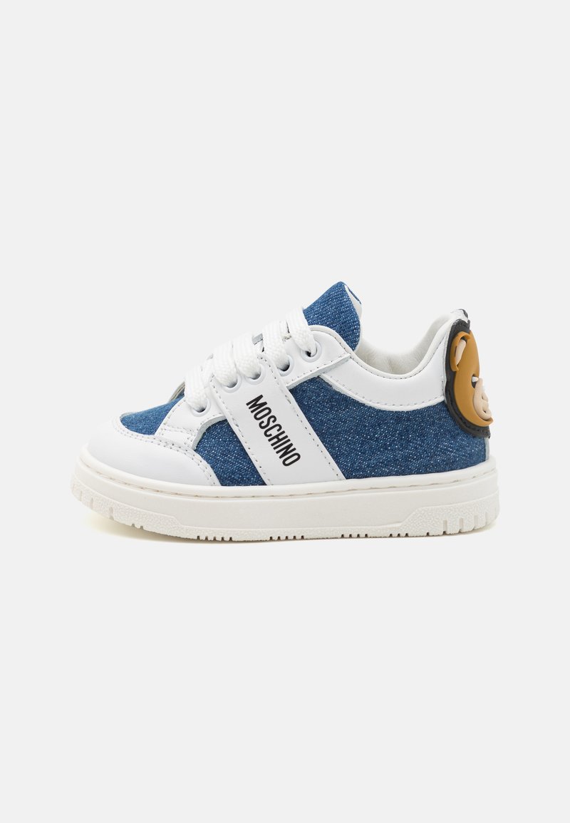 Denim ja valge nahast sneaker koos kummist tallaga, millel on nööriga sulgemine, must logo ja karu kujuline aksessuaar kanna peal.