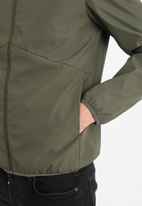 Olivgrön jacka med ett mjukt, lättviktigt tyg, dragkedja fram, elastiska manschetter och sidofickor. Har en ren, figurnära design.