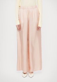 Laiade lõikega pastellroosad püksid, mis on valmistatud siledast, läikivast kangast, millel on elastne vöökoht ja küljetaskud. Kandmiseks valgete teravate jalanõudega.