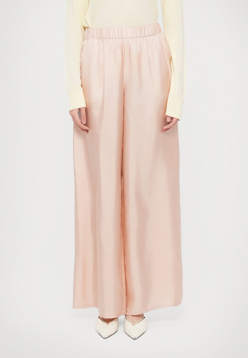 Laiade lõikega pastellroosad püksid, mis on valmistatud siledast, läikivast kangast, millel on elastne vöökoht ja küljetaskud. Kandmiseks valgete teravate jalanõudega.