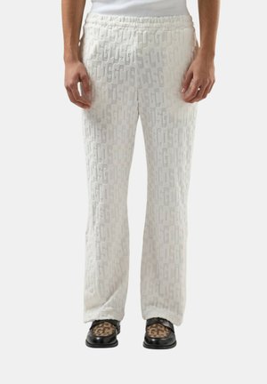 Pantaloni bianchi con trama testurizzata e motivo a logo in rilievo ripetuto, abbinati a mocassini neri con tessuto marrone decorato sulla parte superiore.
