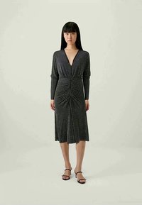 Vestido preto com mangas longas, decote em V e franzido na cintura. Apresenta um padrão texturizado com pequenos pontos brancos. Design midi.