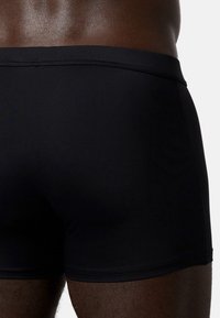 Black swim shorts made from smooth, stretchy fabric, featuring a fitted cut and a wide waistband with minimal stitching details.