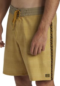 Shorts de bain pour hommes en jaune moutarde avec un motif en plaid texturé, dotés d'une bande latérale noire et d'un cordon jaune à la taille.