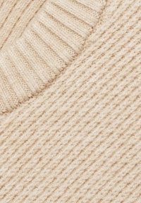 Tissu beige tricoté avec une texture côtelée présentant des bandes larges et étroites alternées, aspect doux et légèrement duveteux.