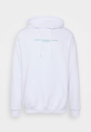 Sweatshirt à capuche blanche avec poches avant et texte bleu clair, associé à un jean bleu clair et des baskets blanches. Design simple et décontracté.