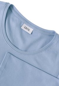 Chemise à col rond bleu clair à manches longues avec une étiquette blanche à l'intérieur du col portant la mention "CECIL."