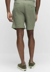 Oliivivihreät, polvipituiset shortsit, joissa on sileä pinta ja kaksi takataskua nappisuljinnoilla. Yhdistetty samanvärisiin vihreisiin kenkiin.