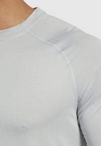 Helles graues Sportshirt aus strukturiertem, atmungsaktivem Material mit dezenten Nahtdetails und rundem Ausschnitt.